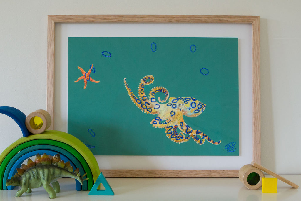An artwork of a blue ringed octopus playing quoits with a starfish. The blue ringed octopus found off the coast of Western Australia. Painted with a predominately teal background. Artwork for boys teens bedroom. An artwork for marine life enthusiast. Gouache on paper, framed in sustainably managed Australian timber frame. Painted by artistic talent Jaelle Pedroli. Inspiration for kid’s bedroom. Styled with dinosaur and wooden toys