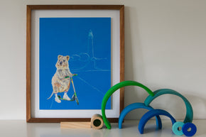 Artwork for a girls bedroom of Western Australian Rottnest Quokka riding a scooter with lighthouse in the background and a predominantly blue background. Framed original gouache painting, painted by Artist Jaelle Pedroli, sits on shelf in Australian themed bedroom.