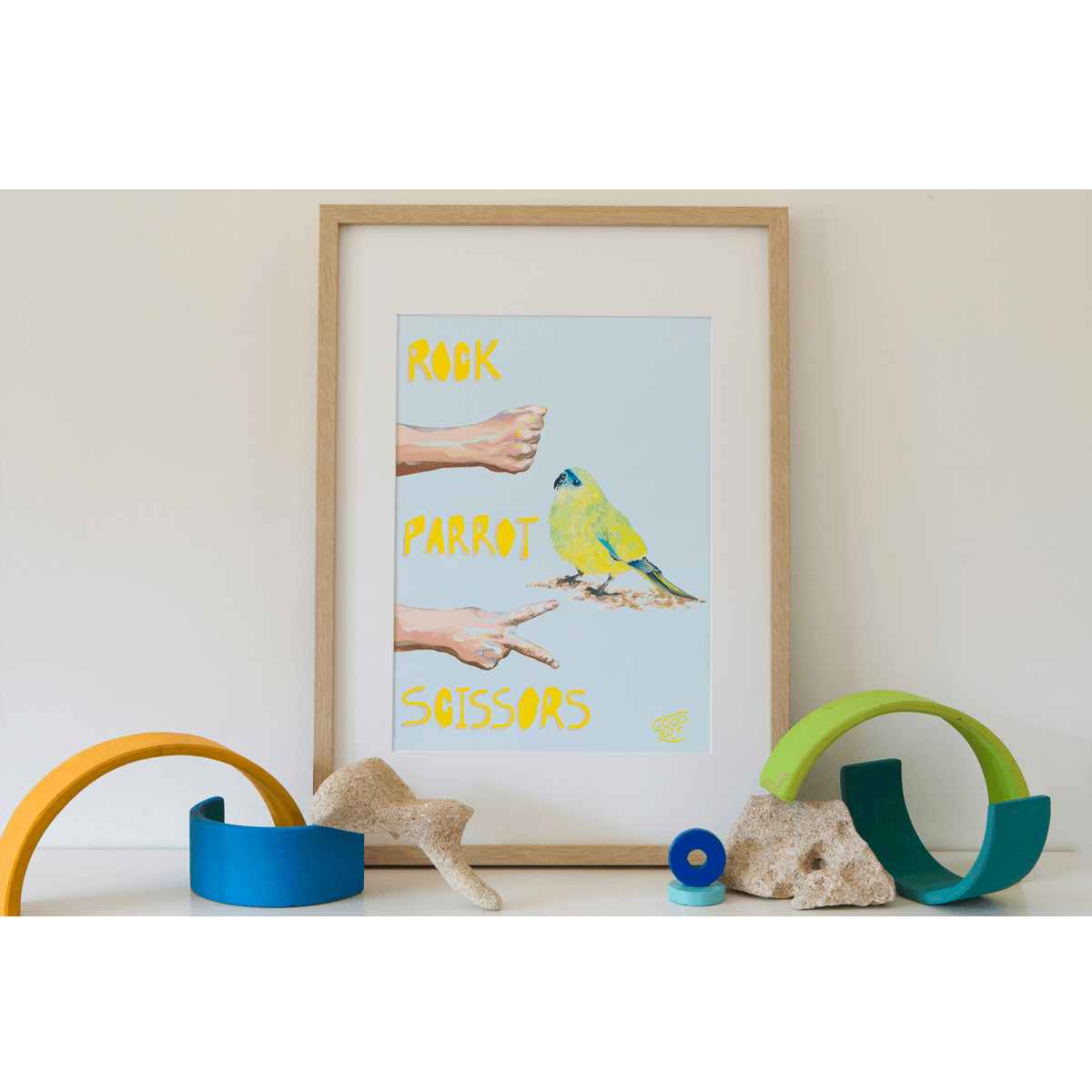 A colourful artwork of the Rottnest Rock Parrot playing a game of rock paper scissors against a pair of hands. Framed original artwork on shelf.