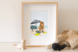 An artwork of a Rottnest quokka wearing a snorkel and flippers beside the ocean, a beach umbrella and a seagull. Framed original painting on shelf.