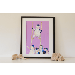 An original artwork of 5 Little Penguins painted by Jaelle Pedroli. Above a waddle of Little Penguins the smallest of them all towers above the heads of all the others on a pair of stilts. The print has a purple background. Framed in a black frame, sitting on a shelf.